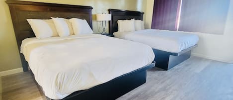 A hotel room with two beds, a wooden headboard, a nightstand, a lamp, and a window with curtains.
