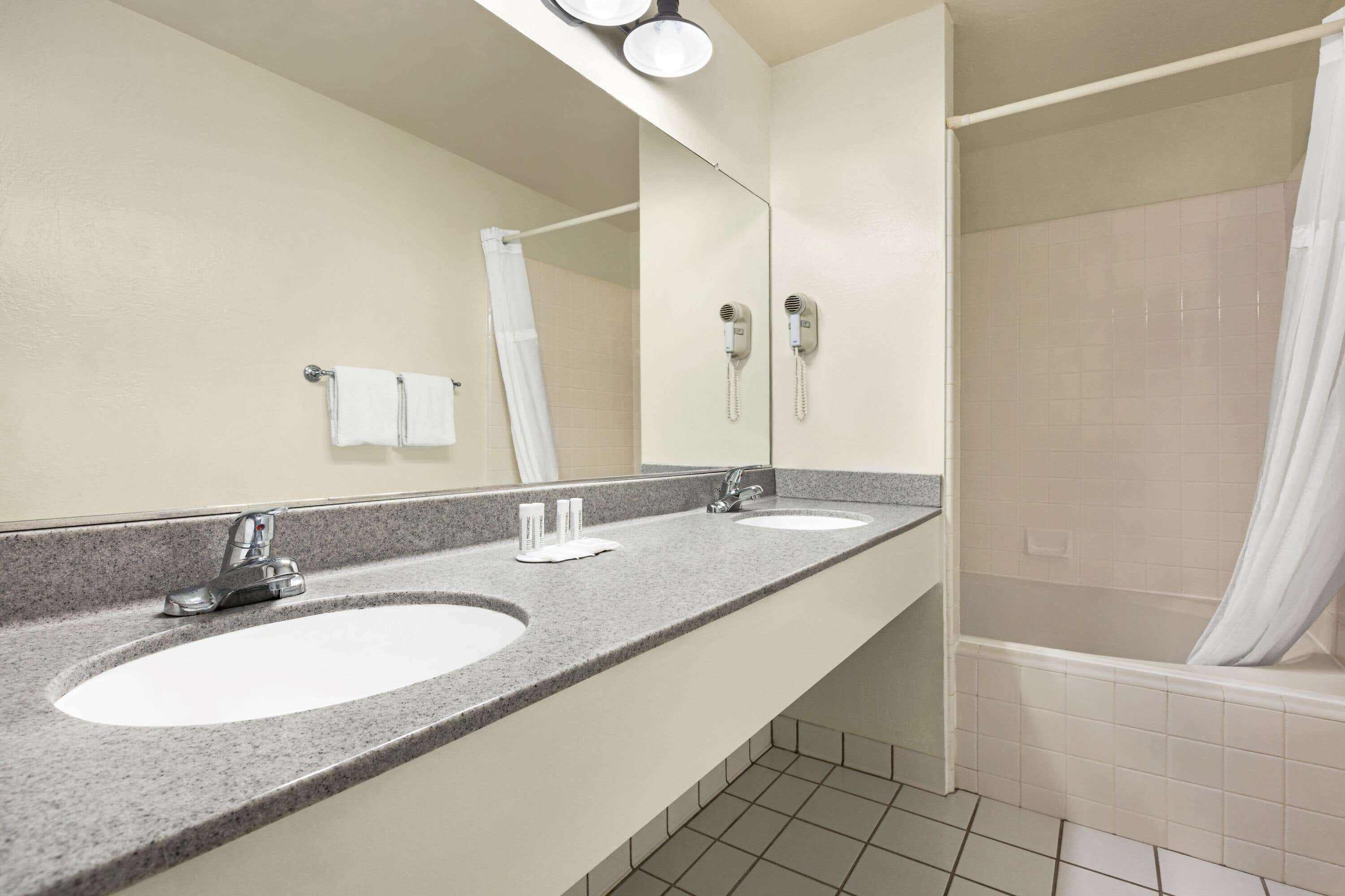 A bathroom with two sinks, a mirror, a shower, and a towel rack.