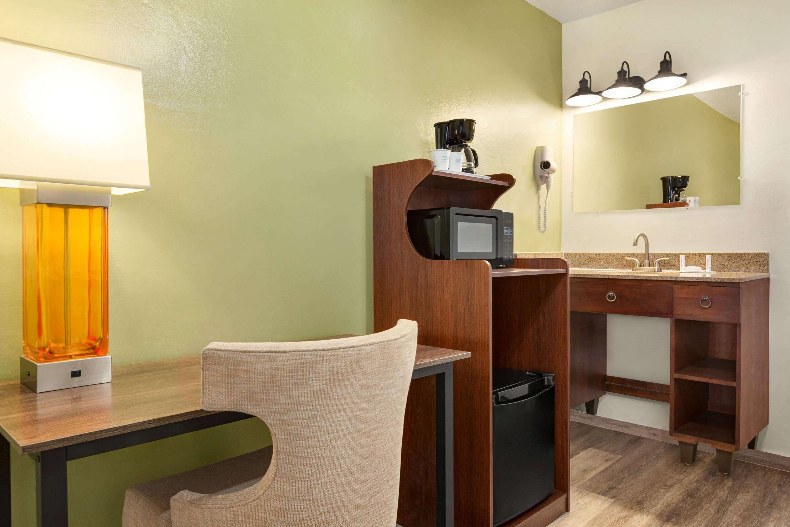 Un baño de hotel con un tocador de madera, un lavamanos, un espejo, un secador de pelo y una cafetera.