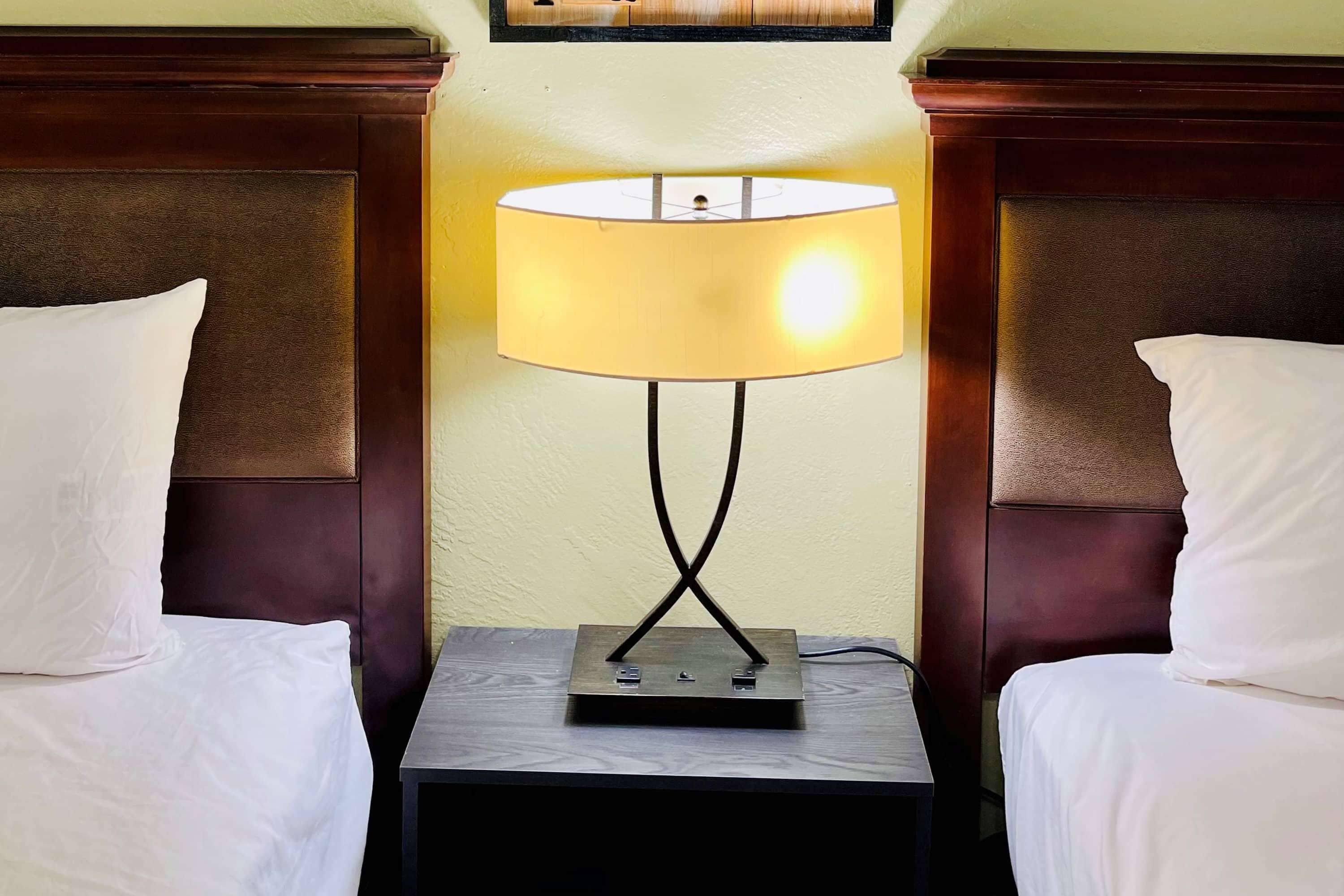 A hotel room with a bed, a nightstand with a lamp, and a wall-mounted picture.