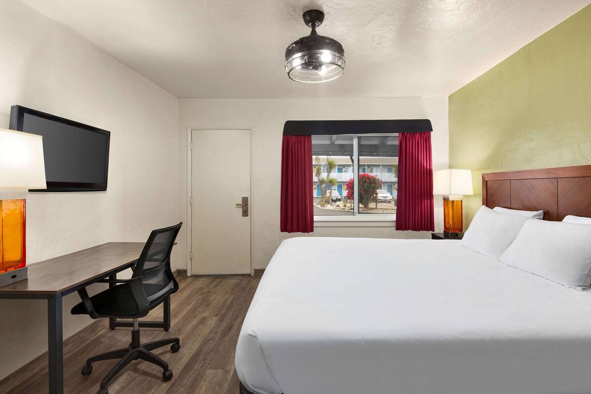A hotel room with a bed, desk, chair, television, and a window with curtains.