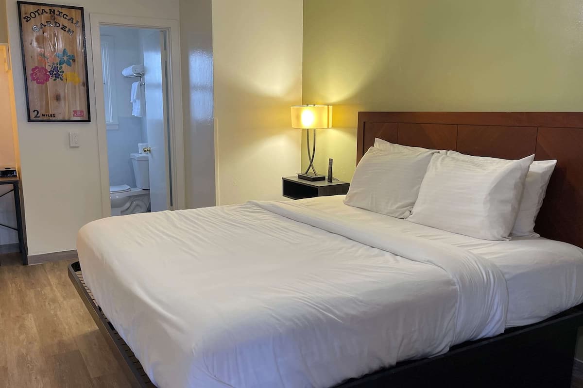 A hotel room with a large bed, a nightstand with a lamp, a wooden headboard, and a poster on the wall.
