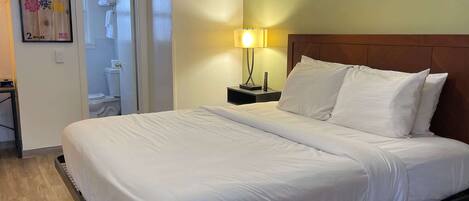 A hotel room with a large bed, a nightstand with a lamp, a wooden headboard, and a poster on the wall.