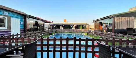 A swimming pool with a wooden fence, surrounded by grass and wicker chairs.