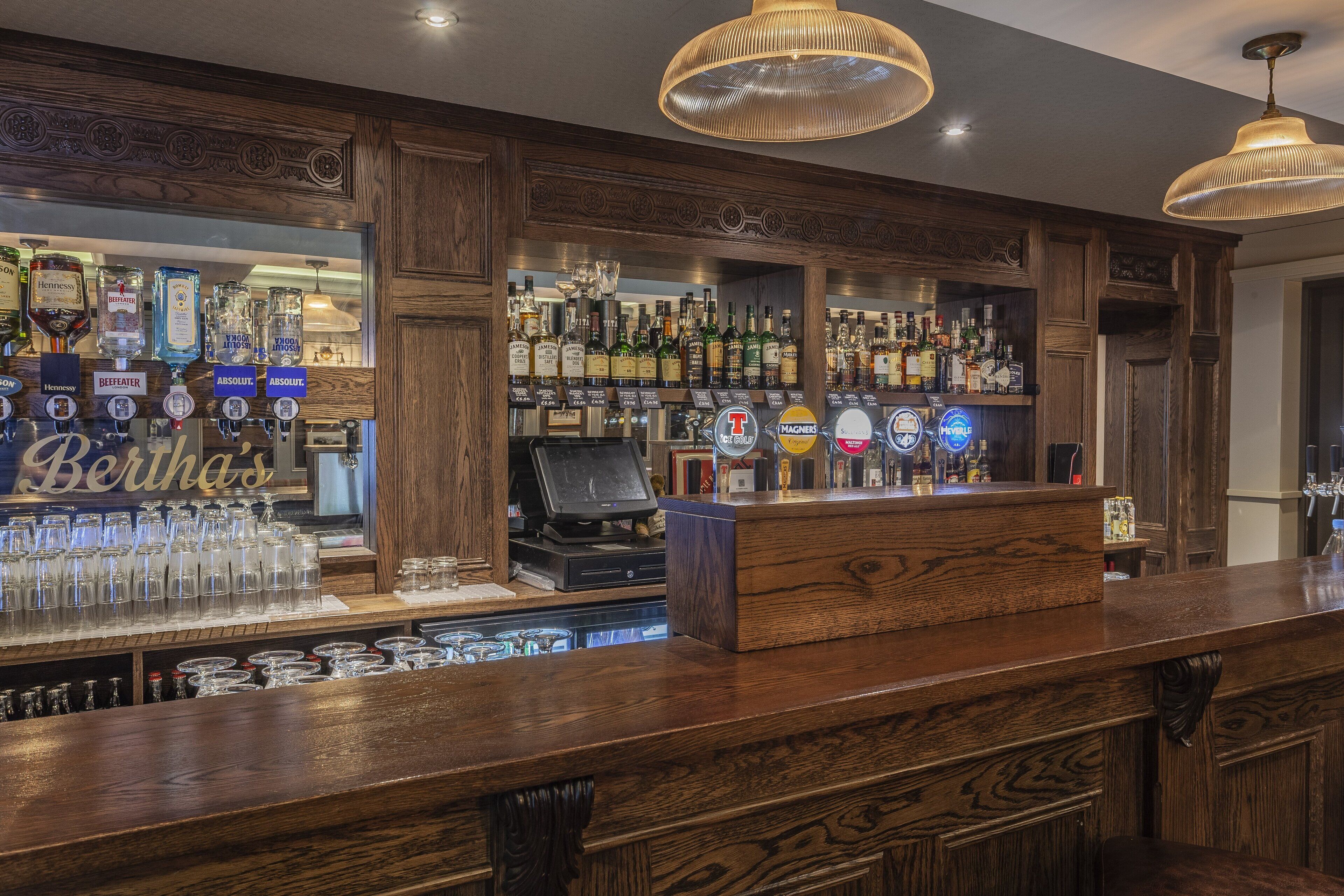 Een bar met houten inrichting, een kassa en verschillende flessen drank.
