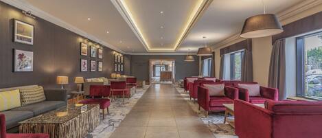 A spacious lobby with a central corridor, red seating, and framed artwork on the walls.