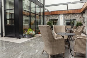 Relax in the serene outdoor seating area with wicker furniture and a stone-tiled floor, surrounded by lush greenery.