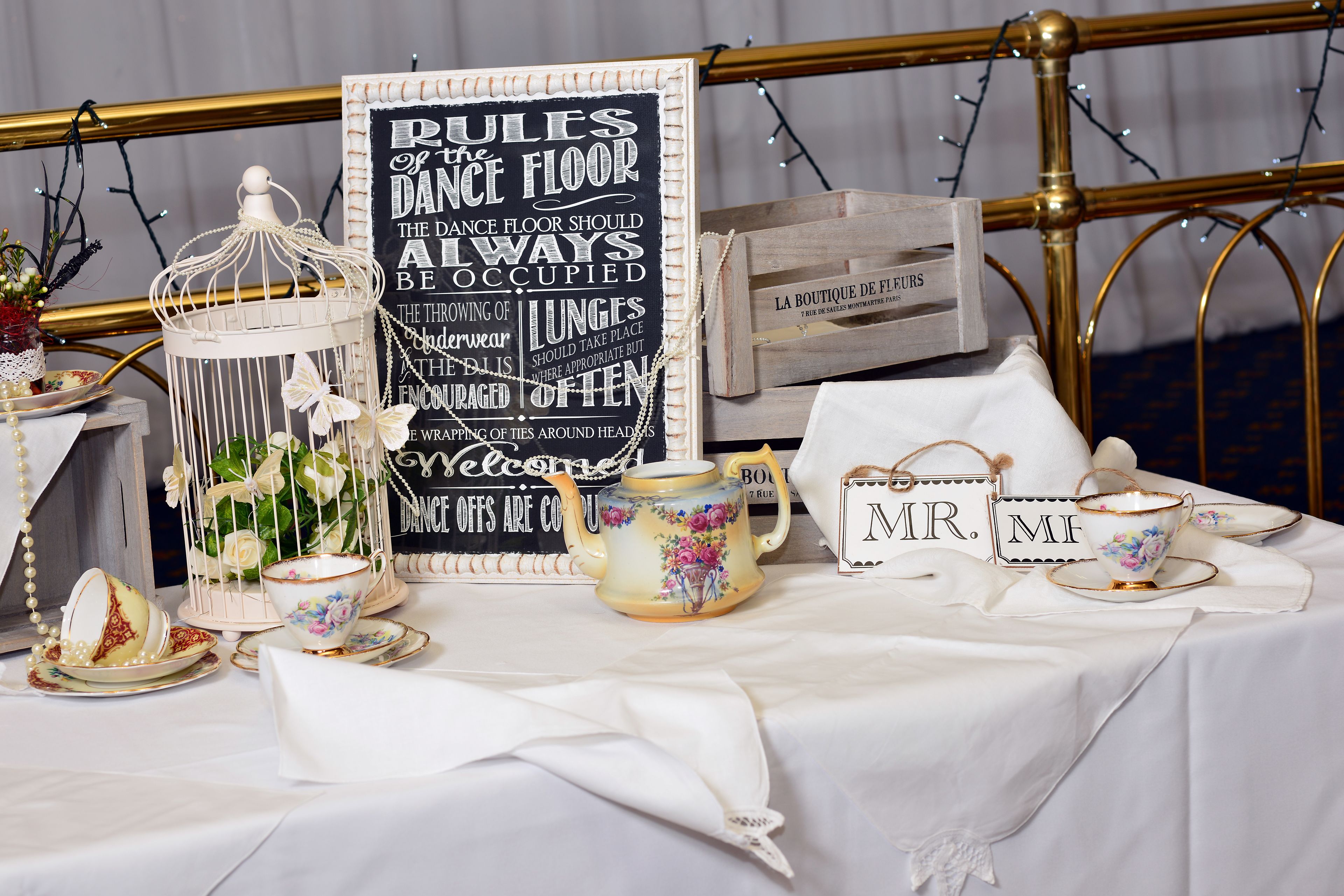 A table set with tea cups, a teapot, and a sign with dance floor rules.