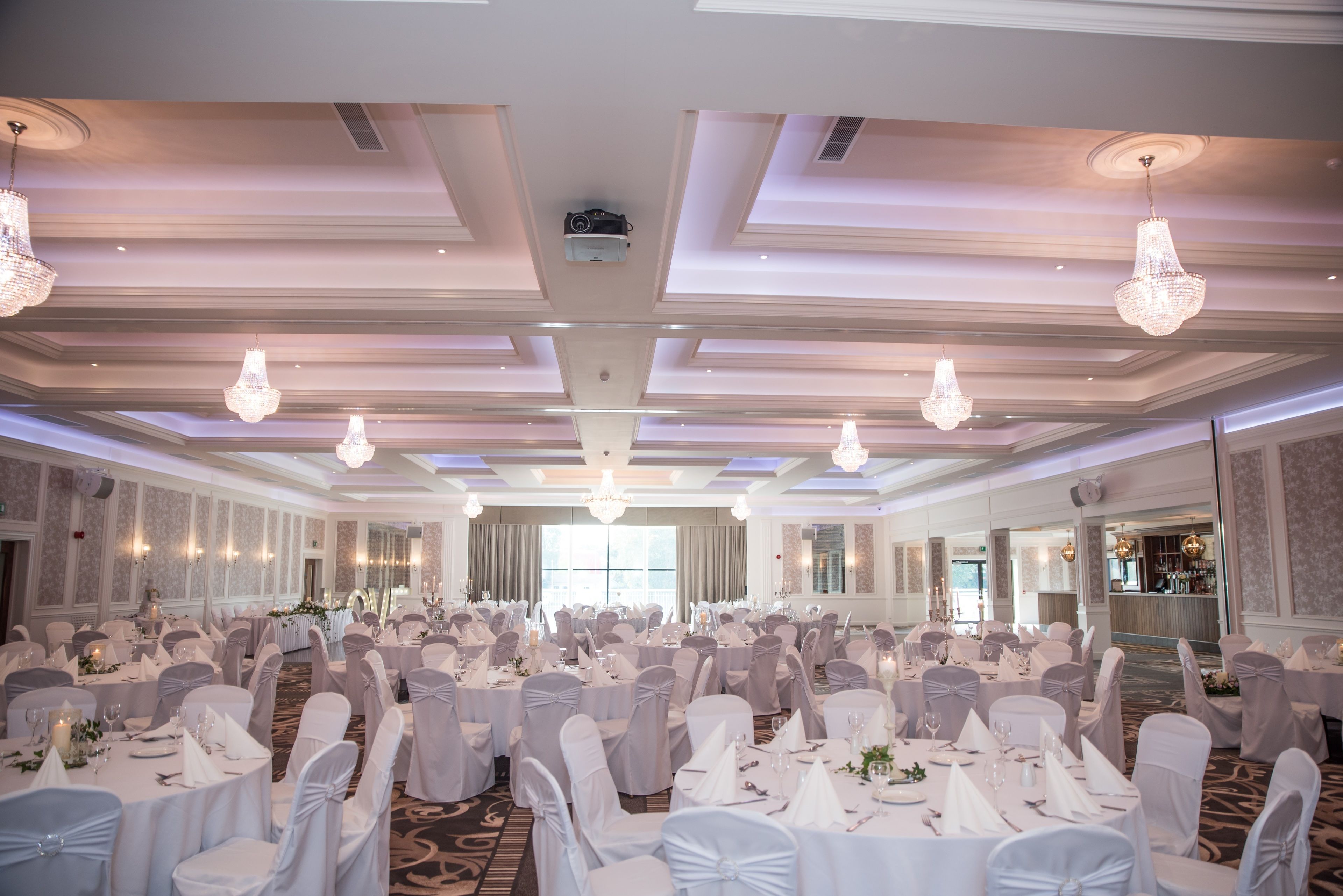 A banquet hall with rows of round tables, white tablecloths, and chairs with white sashes.