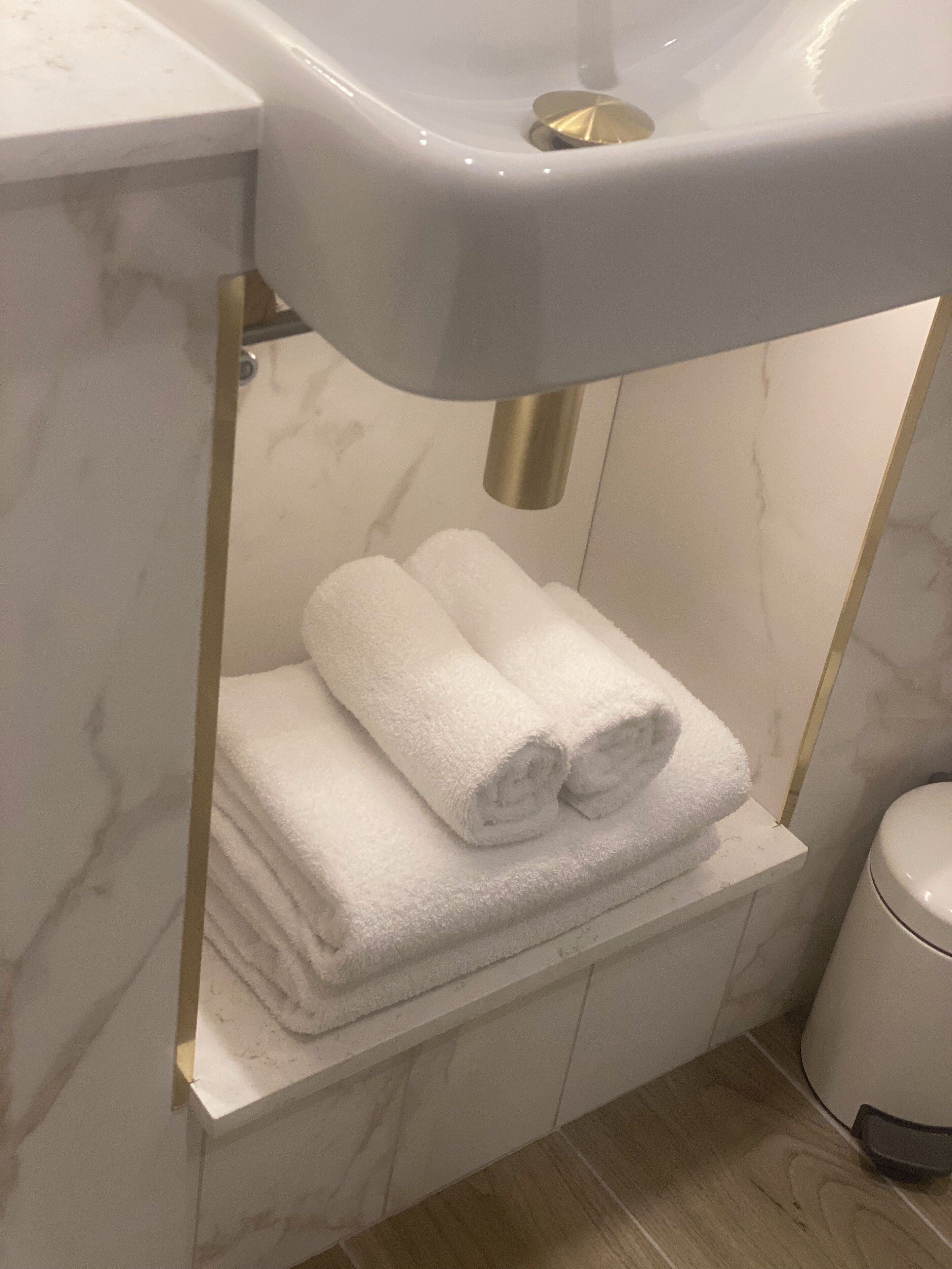 A bathroom with a white sink, marble walls, and a towel rack with folded towels.