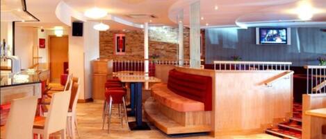A modern hotel lobby with a wooden reception desk, a seating area with red benches, and a staircase with red carpet.