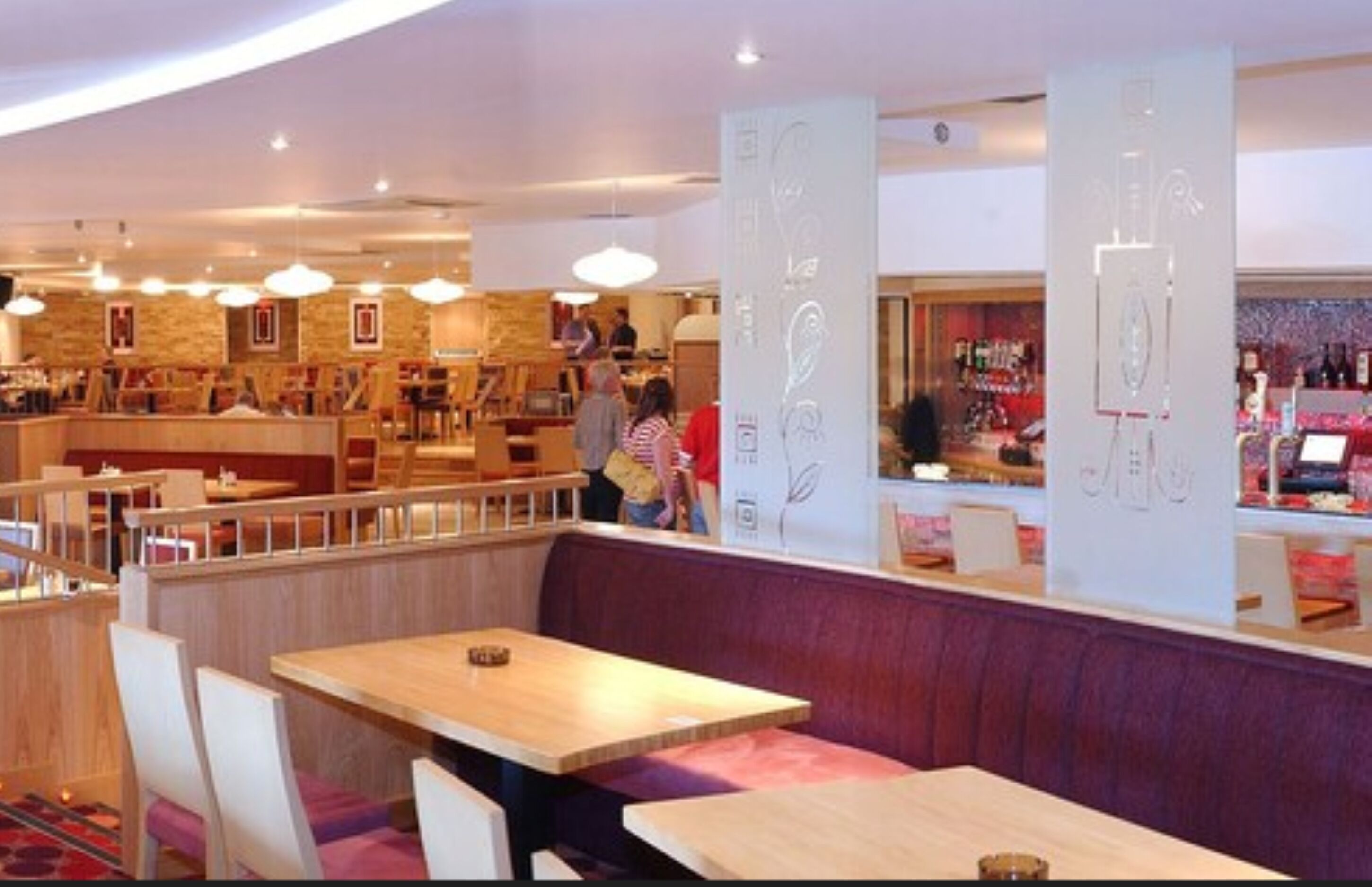 A restaurant with wooden tables and purple booths, a bar area in the background, and a modern interior design.