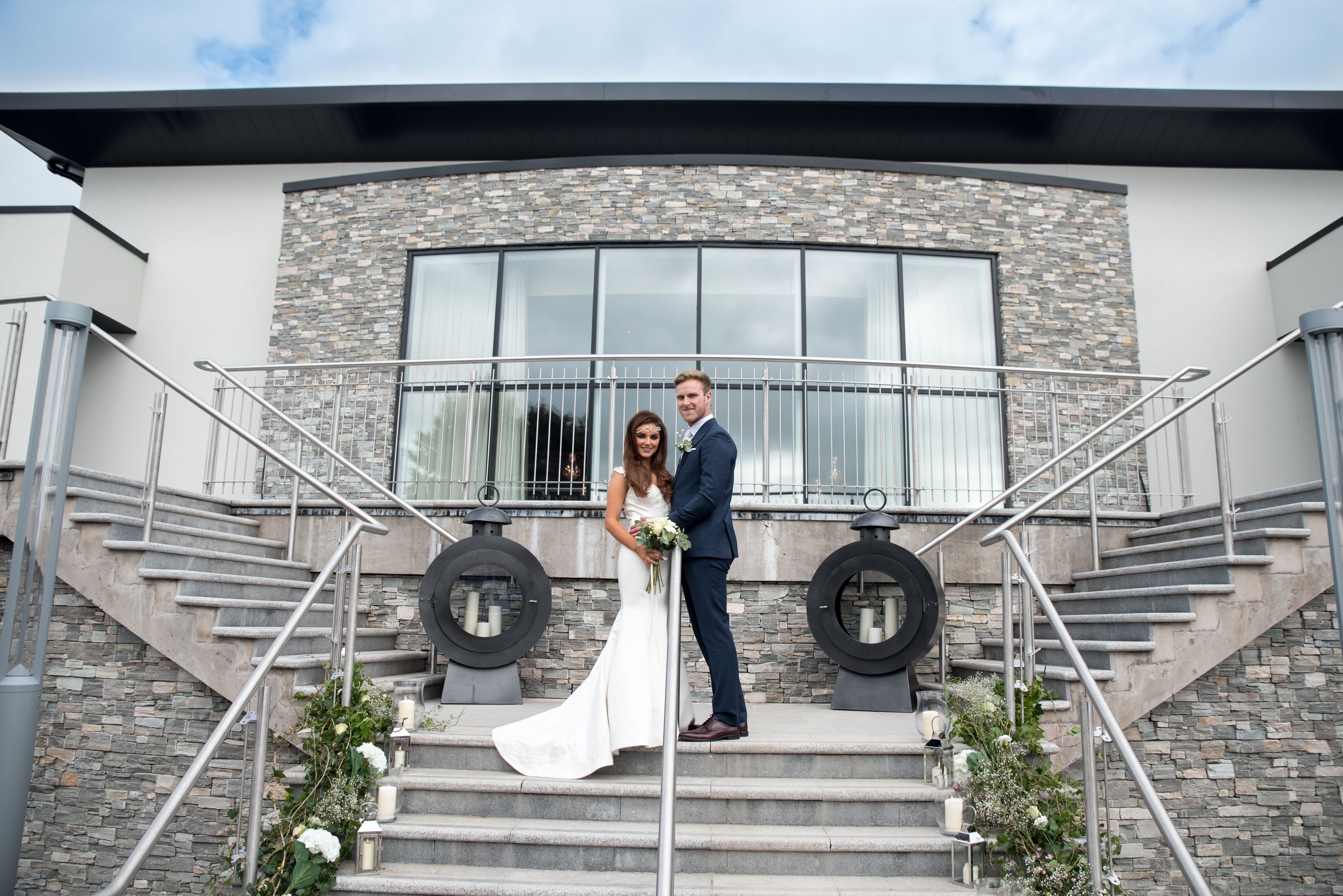 A couple on a staircase with a stone facade and large windows.