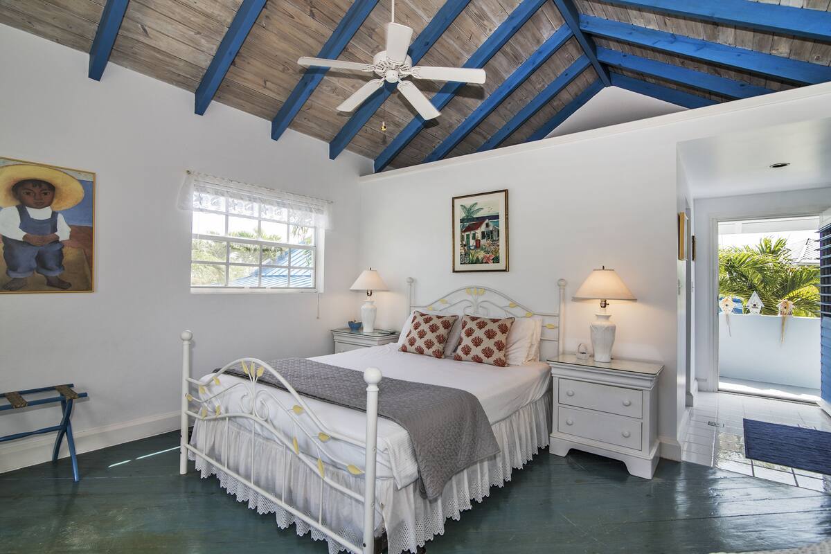 Une chambre à coucher avec un lit, des tables de chevet, un ventilateur de plafond et une fenêtre.