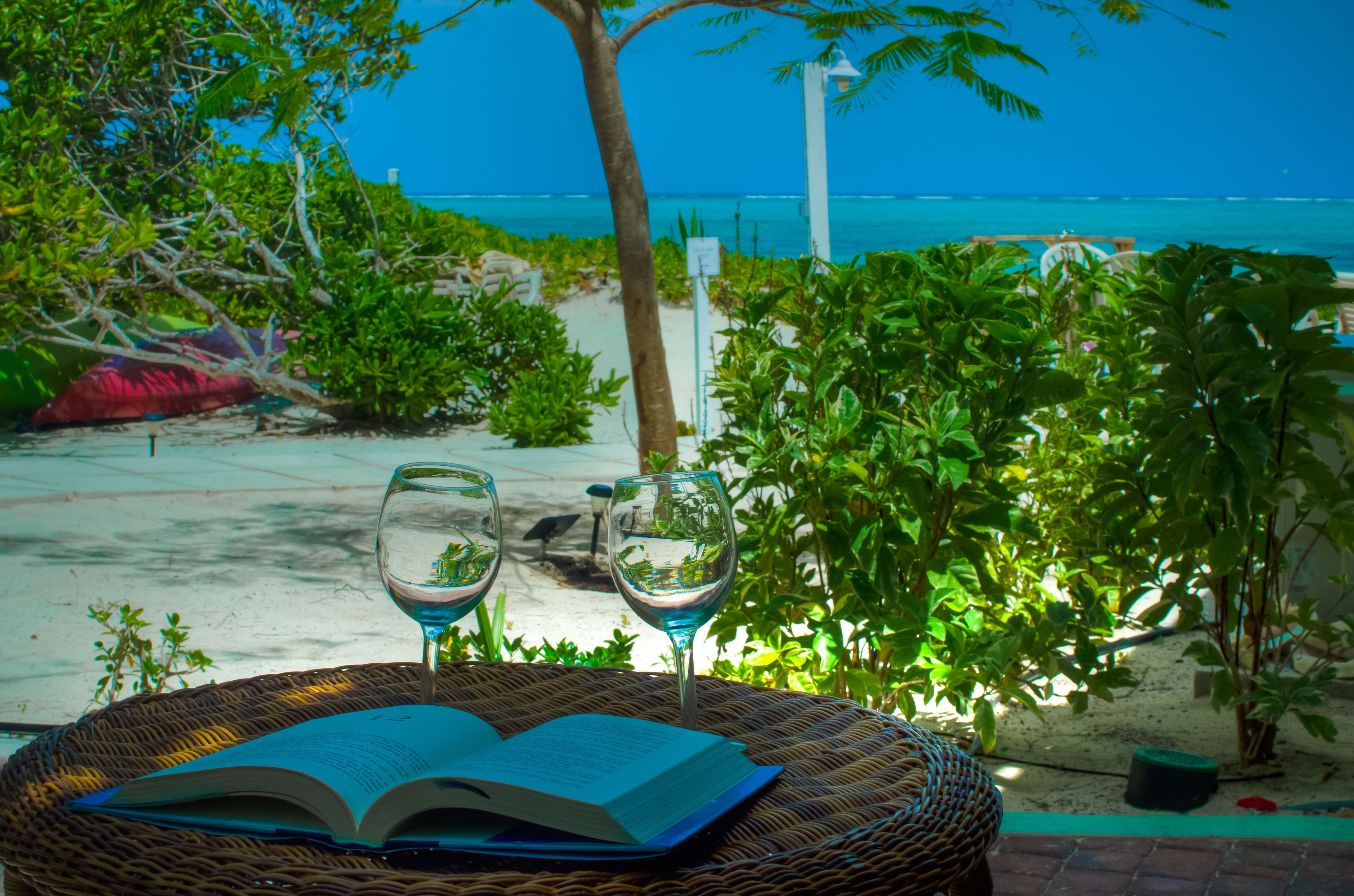Una silla de mimbre con un libro abierto y dos copas de vino en una terraza con vista a la playa.