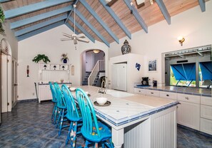 Une cuisine spacieuse avec un grand îlot central, des chaises bleues et un ventilateur de plafond.
