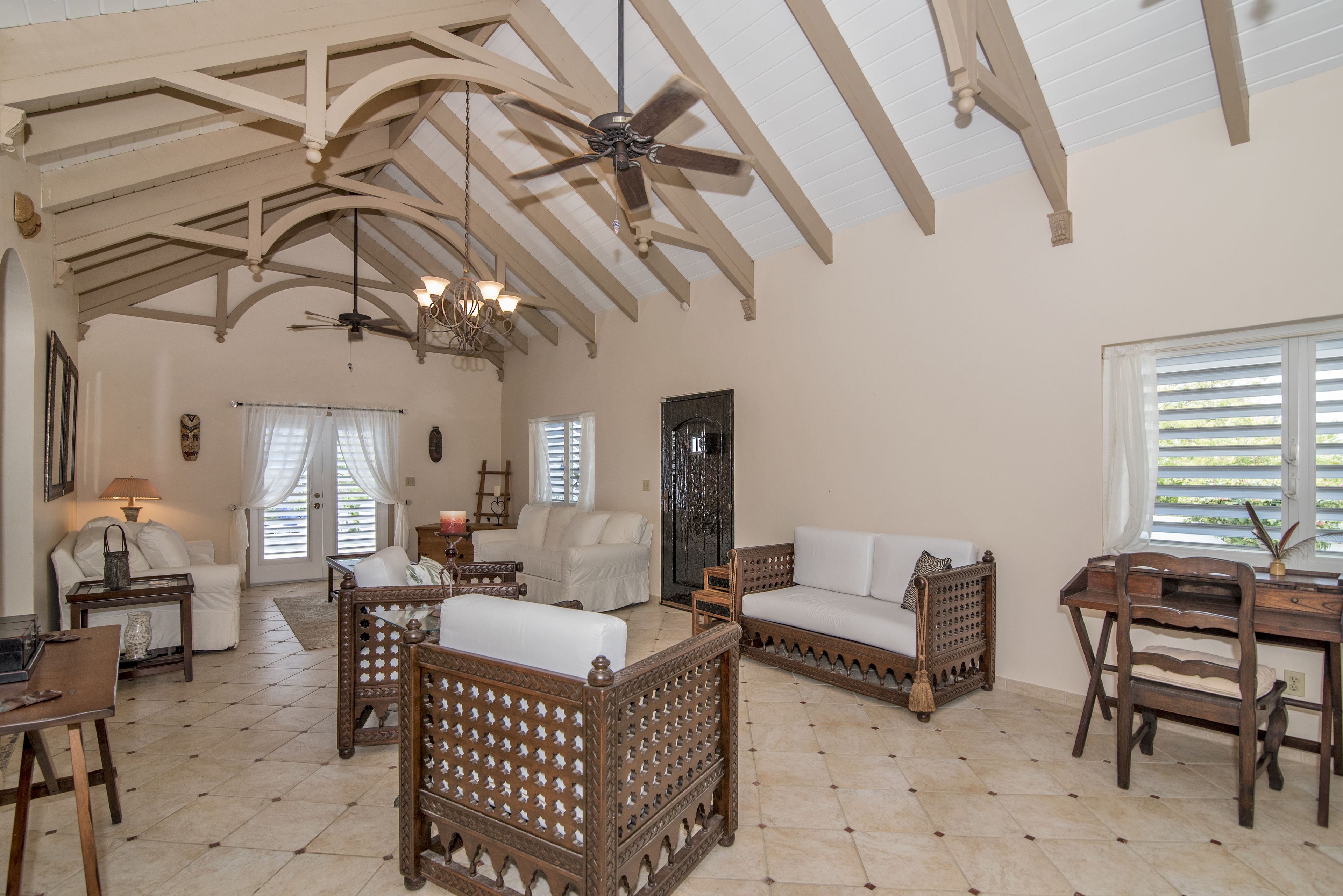 A spacious living room with high ceilings, wooden furniture, and a chandelier.