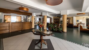 Un vestíbulo espacioso con una mesa central de vidrio, una recepción de madera y grandes columnas.