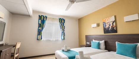 A hotel room with two beds, a desk, a chair, a ceiling fan, and artwork on the walls.