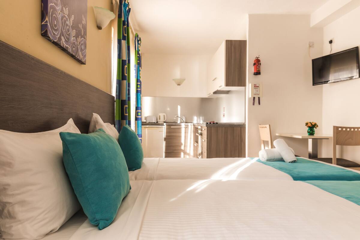 Une chambre d’hôtel équipée d’un lit, d’un bureau, d’une chaise, d’une télévision et d’une kitchenette.