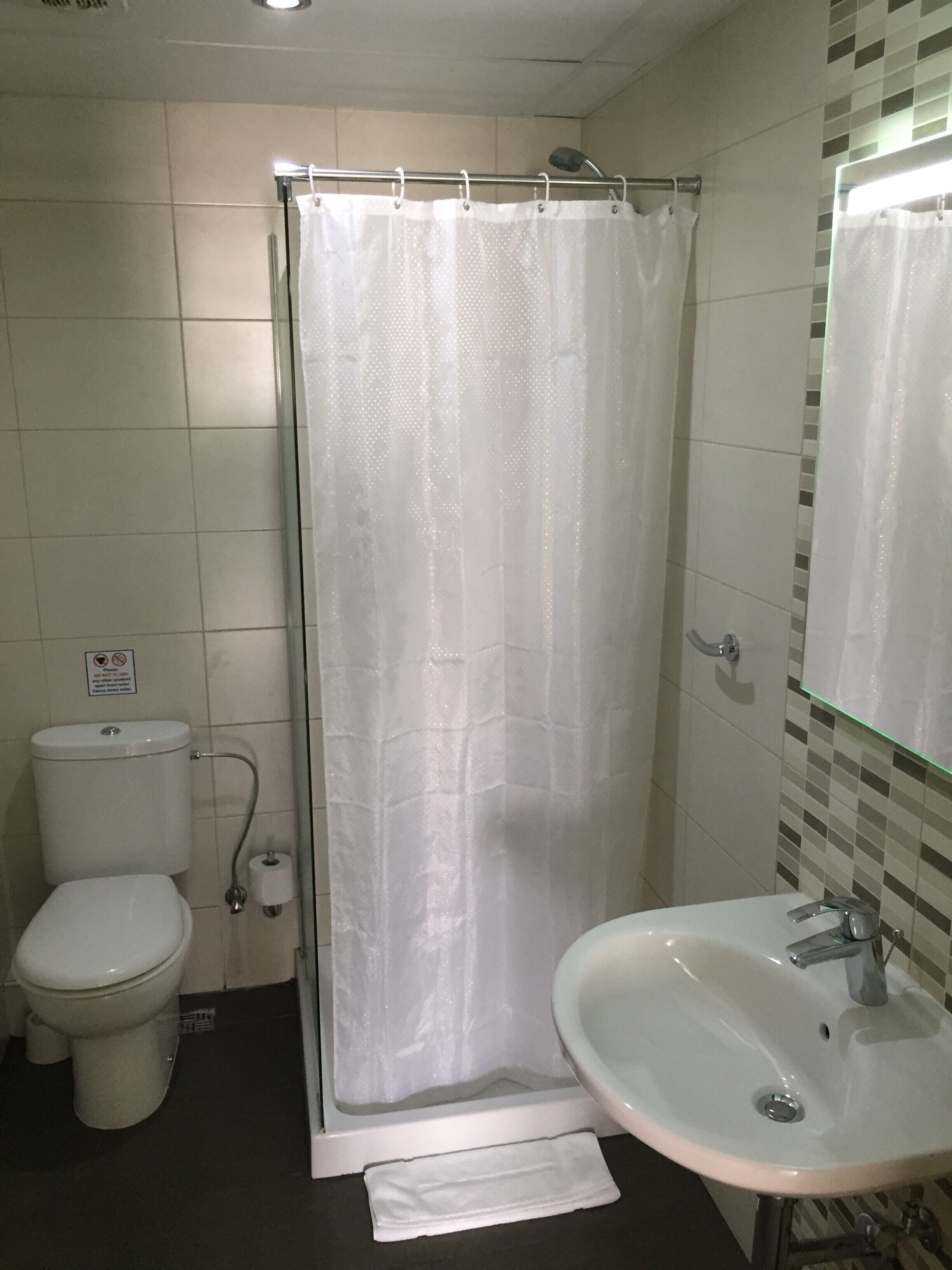 Kylpyhuone, jossa on wc, suihkuverho, pesuallas ja peili.