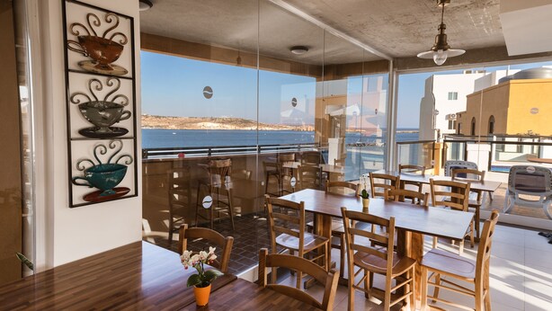 Un comedor con mesas y sillas de madera, vista al mar y un balcón con barandilla.