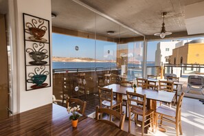 Un comedor con mesas y sillas de madera, vista al mar y un balcón con barandilla.