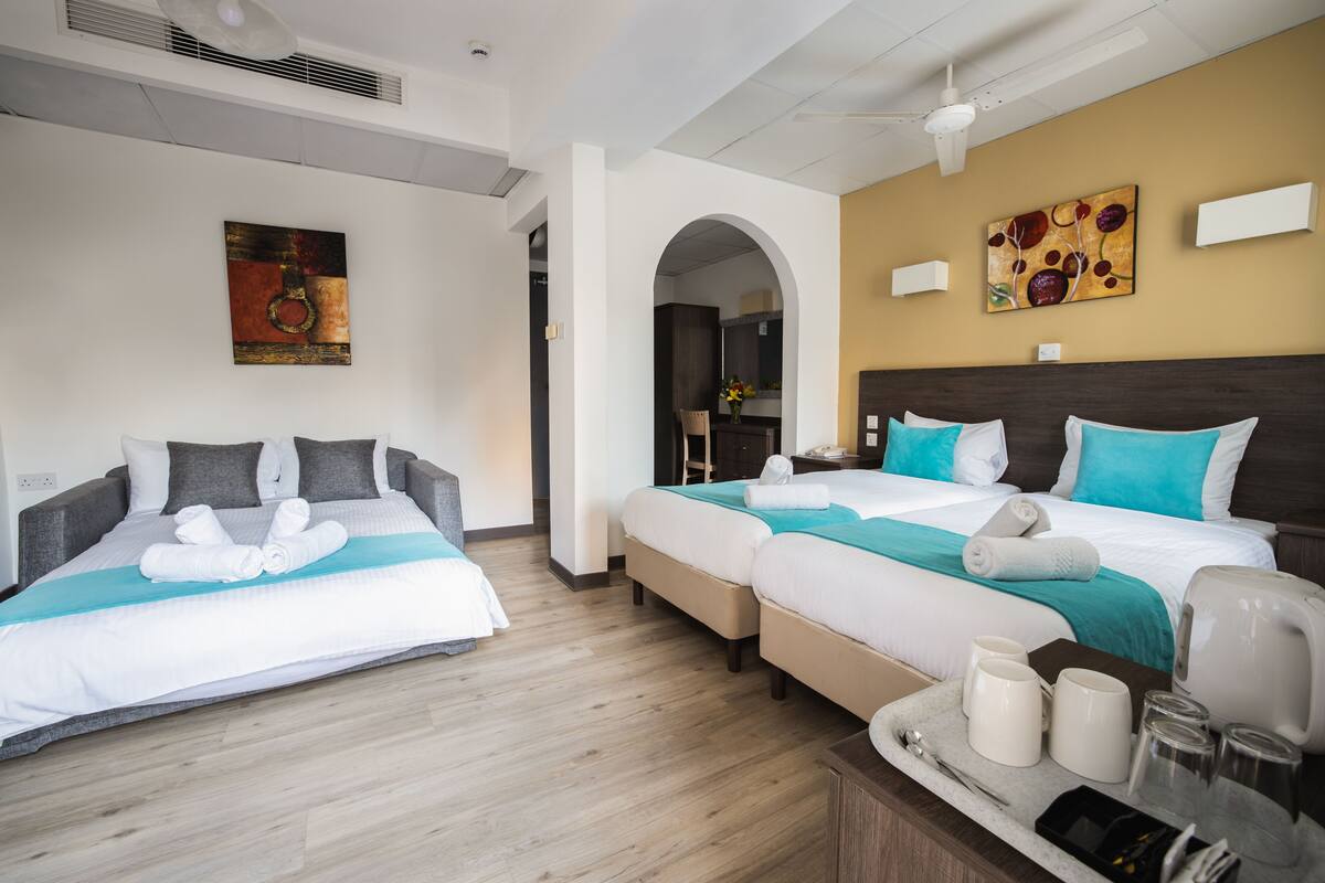 Une chambre d’hôtel avec deux lits, une kitchenette et une salle de bain visible à travers une arche.