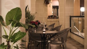 Un comedor con una mesa redonda, sillas, plantas en macetas y velas.