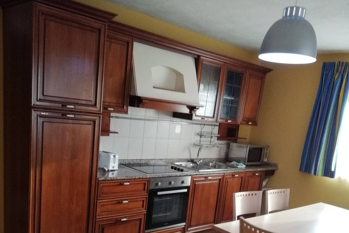 Une cuisine avec des meubles de rangement en bois, un four à micro-ondes, une cuisinière et une table à manger avec des chaises.