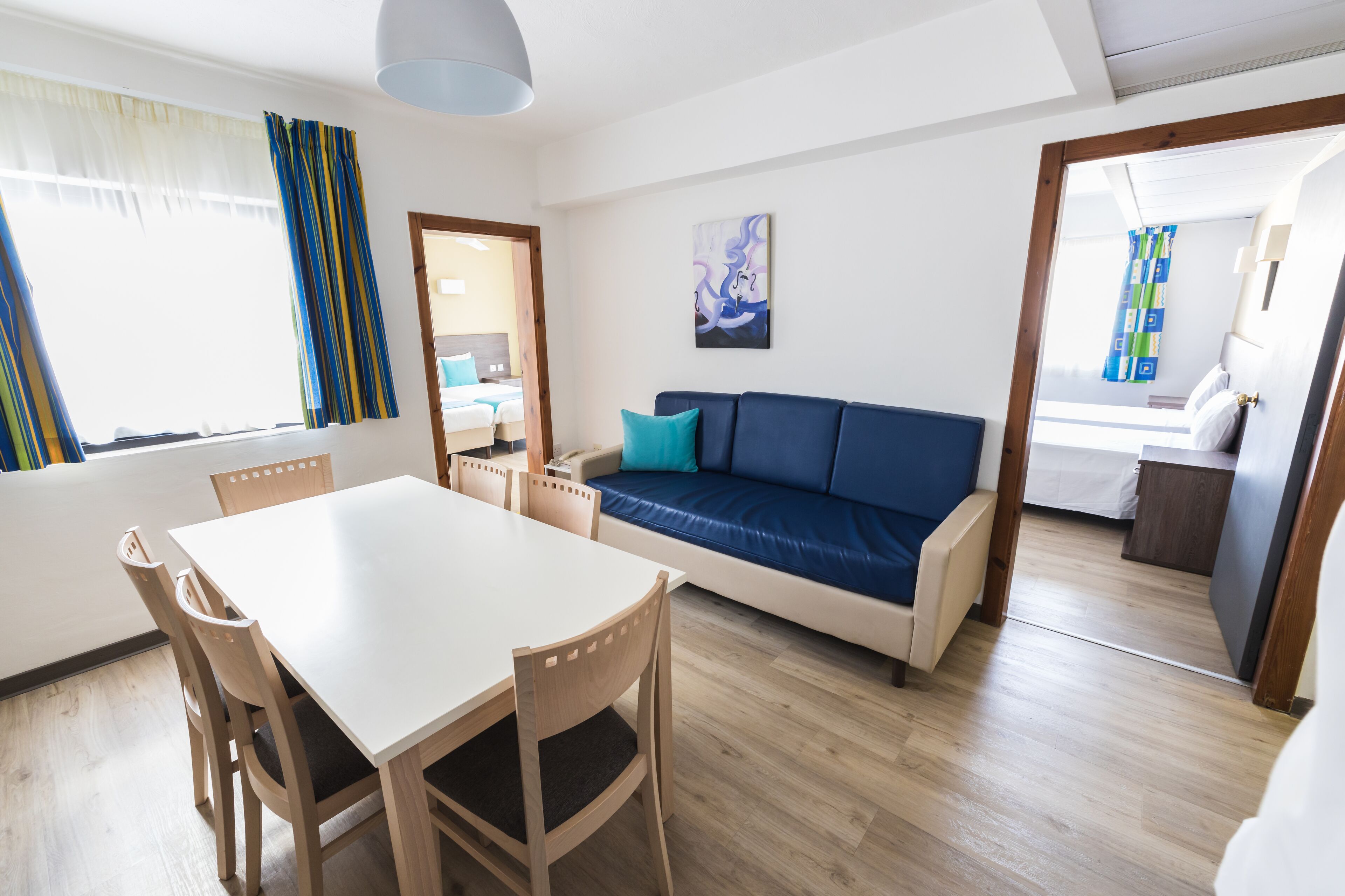En moderne stue med spisebord, træstole, en blå sofa og et maleri på væggen.