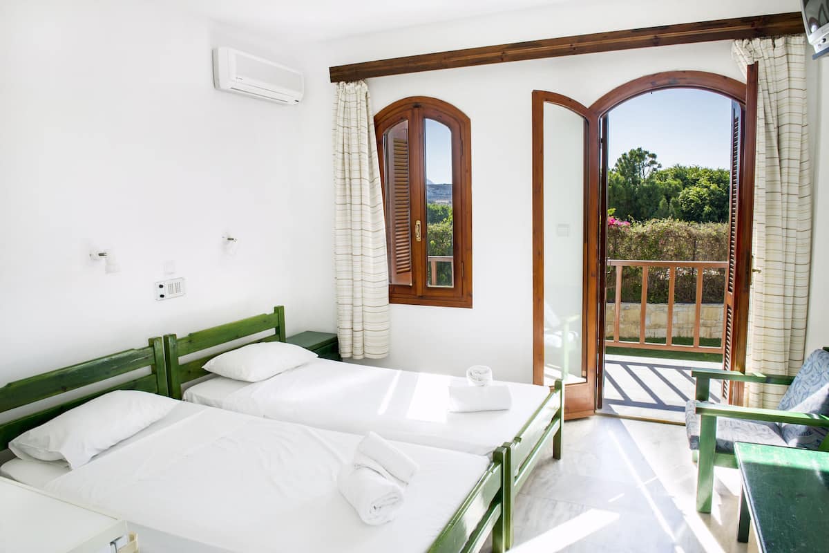 A hotel room with two beds, a balcony with a view, and a wooden-framed window.