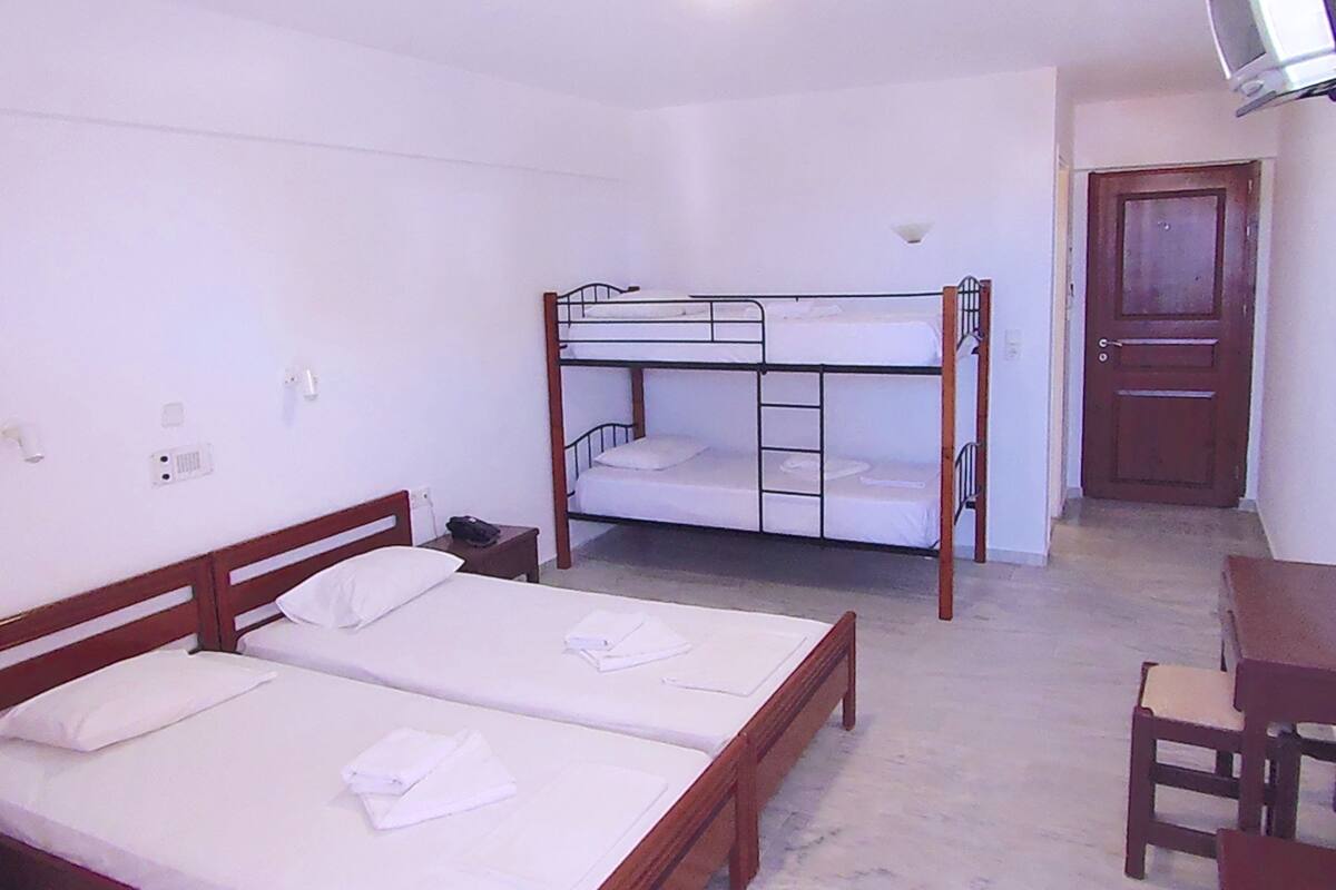 A room with two single beds, a bunk bed, a desk with a chair, a television, and a door.