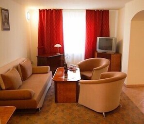 A living room with a sofa, armchair, and a small table with a lamp. A television is on a stand against the wall.