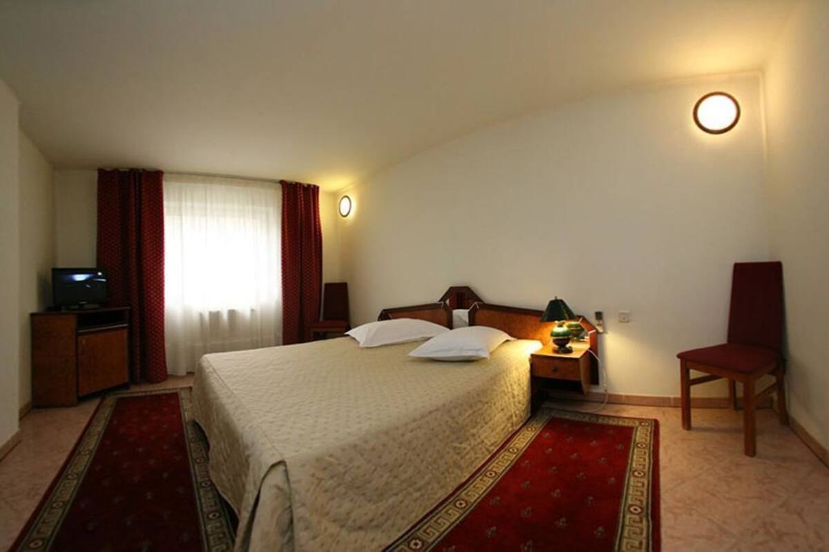 A hotel room with a bed, a desk with a lamp, a TV, and a chair.