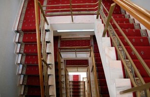 A grand staircase with red carpeted steps and golden handrails, leading to an upper floor.