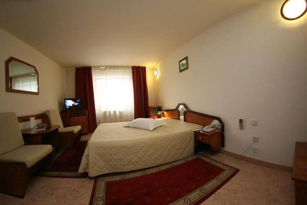 A hotel room with a bed, a desk, a chair, a television, and a window with curtains.