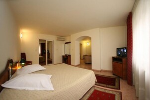 A hotel room with a large bed, a television, a desk, and a bathroom visible through an archway.