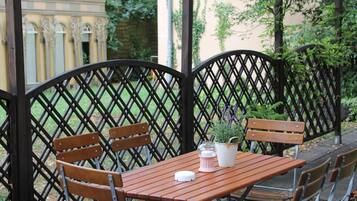 Una mesa de madera con sillas, una planta en maceta y una jarrón blanco en un patio con un cerramiento de celosía.
