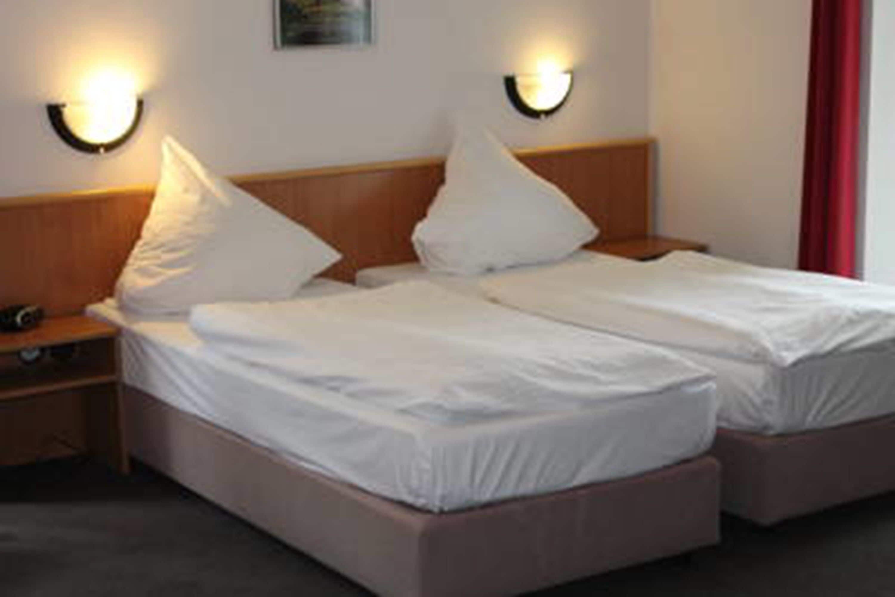 A double bed with two pillows and a wooden headboard. There are two wall-mounted light fixtures on either side of the bed.