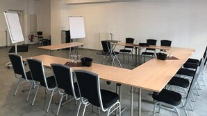 Un salón de conferencias con largas mesas, sillas negras y rotafolios blancos.