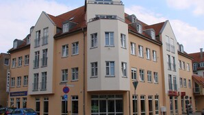 Un hotel de varios pisos con una torre angular destacada, ventanas amplias y un cartel que indica una zona de estacionamiento.