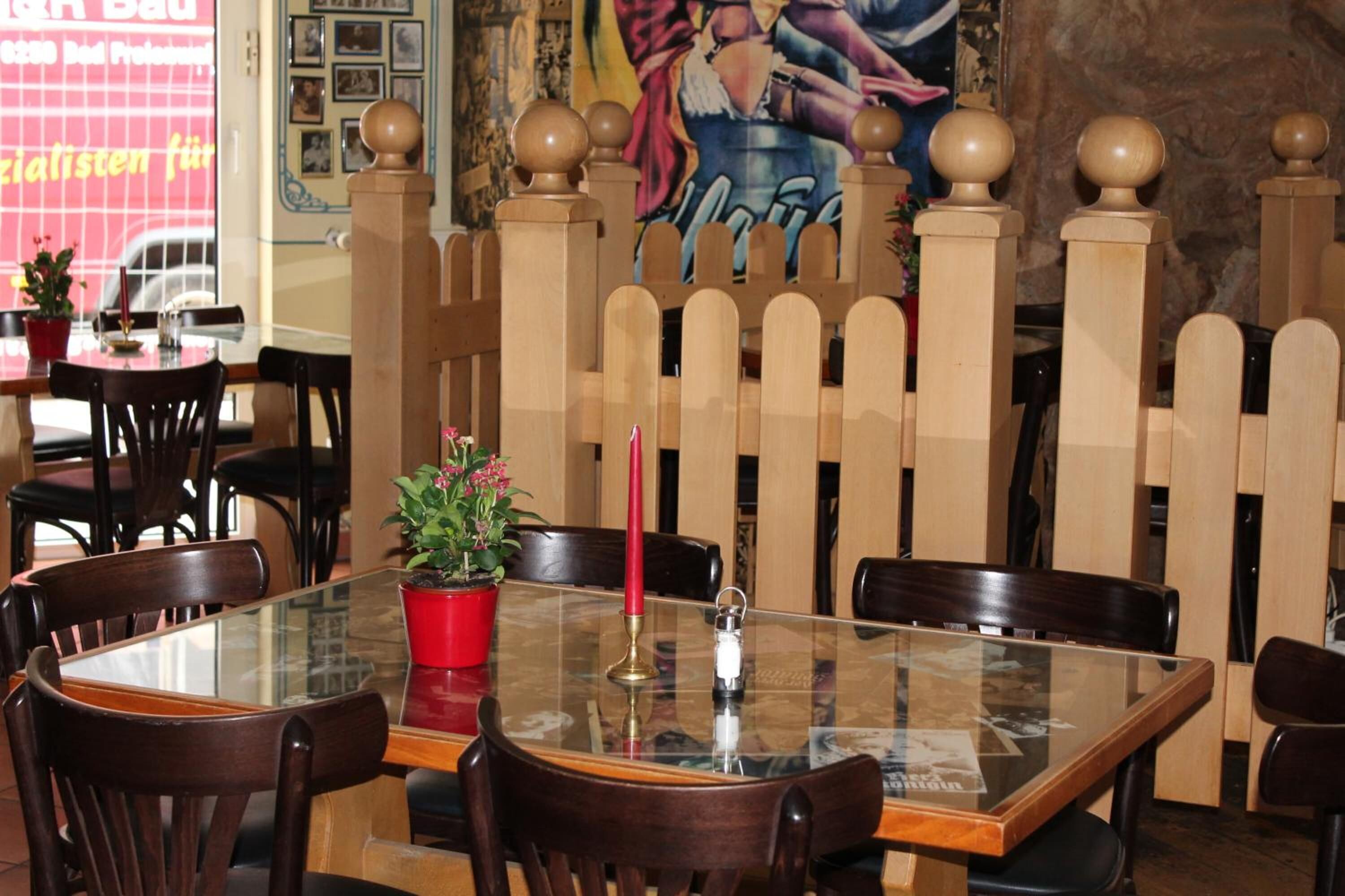 Zona pranzo con tavolo in vetro, sedie in legno, una candela rossa e una pianta in vaso.