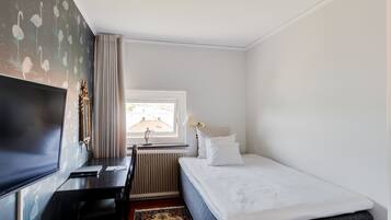 A hotel room with a bed, a desk, a television, a window with curtains, and a radiator.