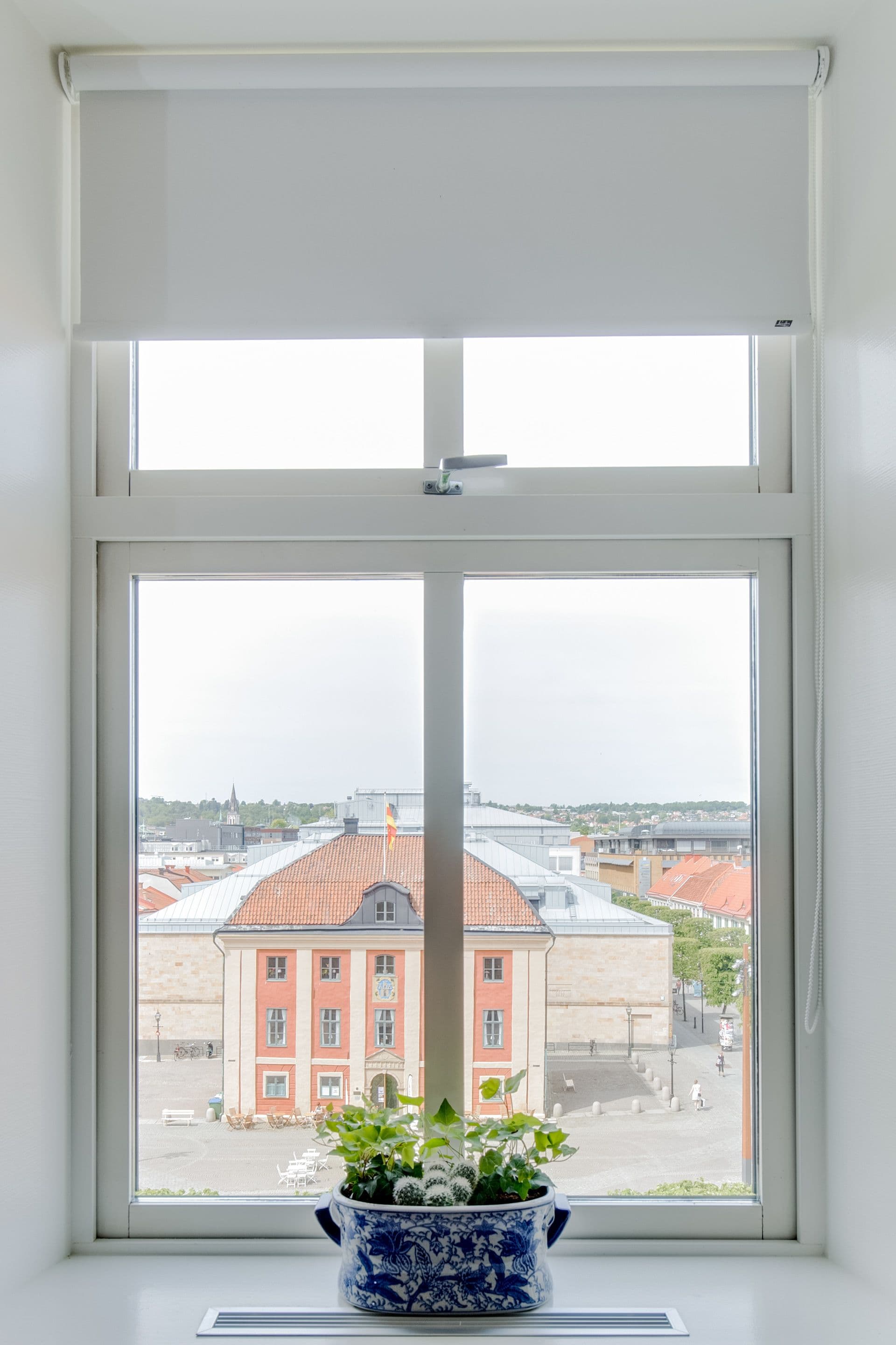 Une fenêtre donnant sur un bâtiment avec un toit rouge et un vase bleu et blanc orné de fleurs, posé sur le rebord de la fenêtre.