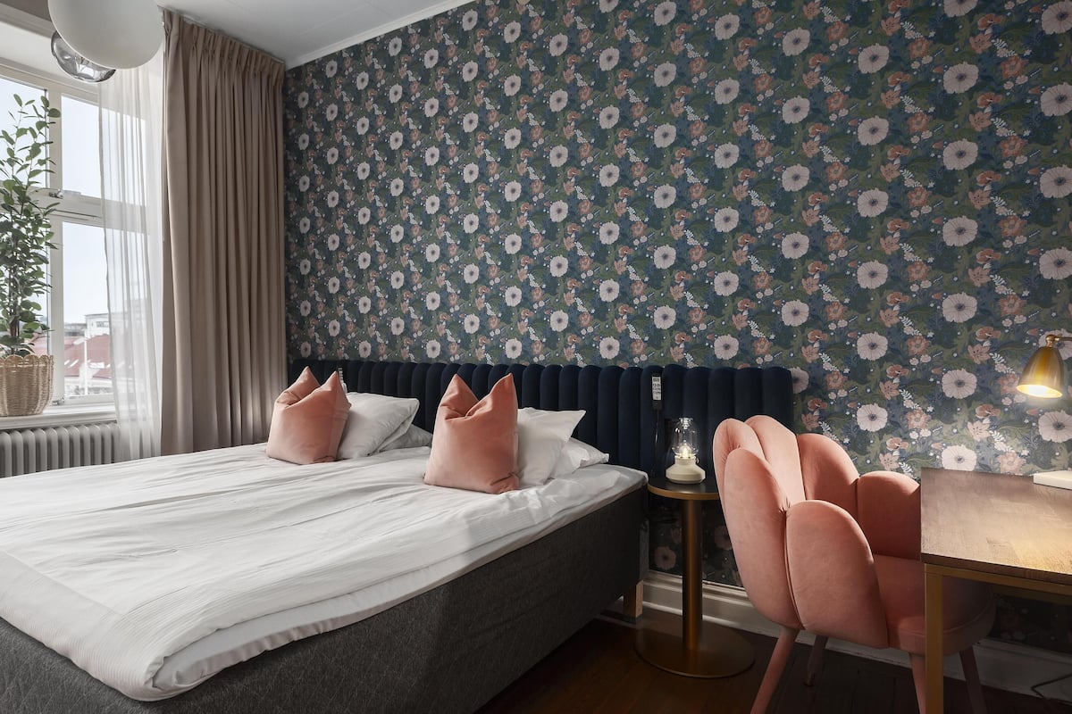 Un dormitorio con cama, una silla, una mesa y un papel tapiz floral en la pared.