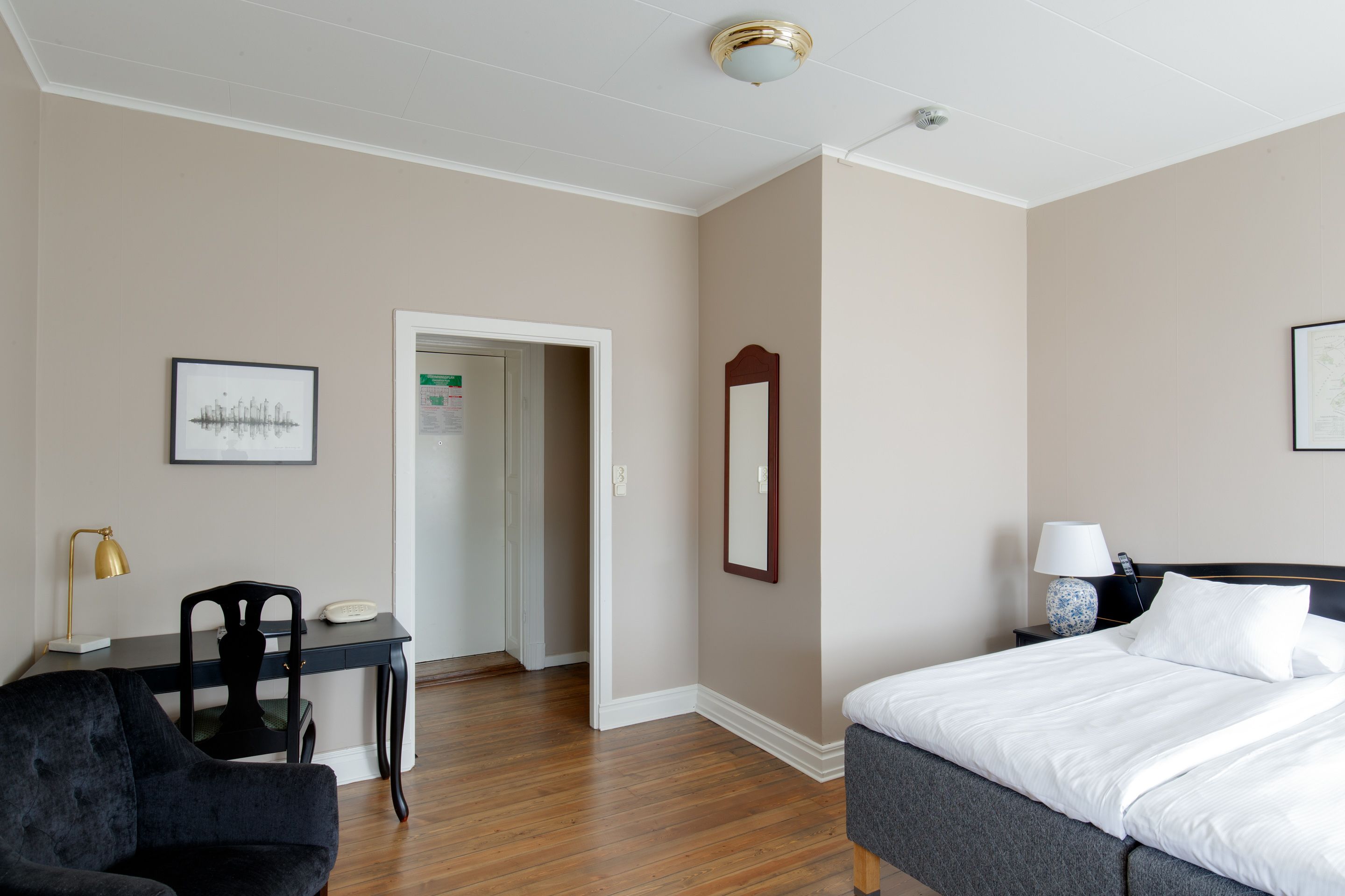 A hotel room with a bed, a desk, a chair, a nightstand, and a mirror.