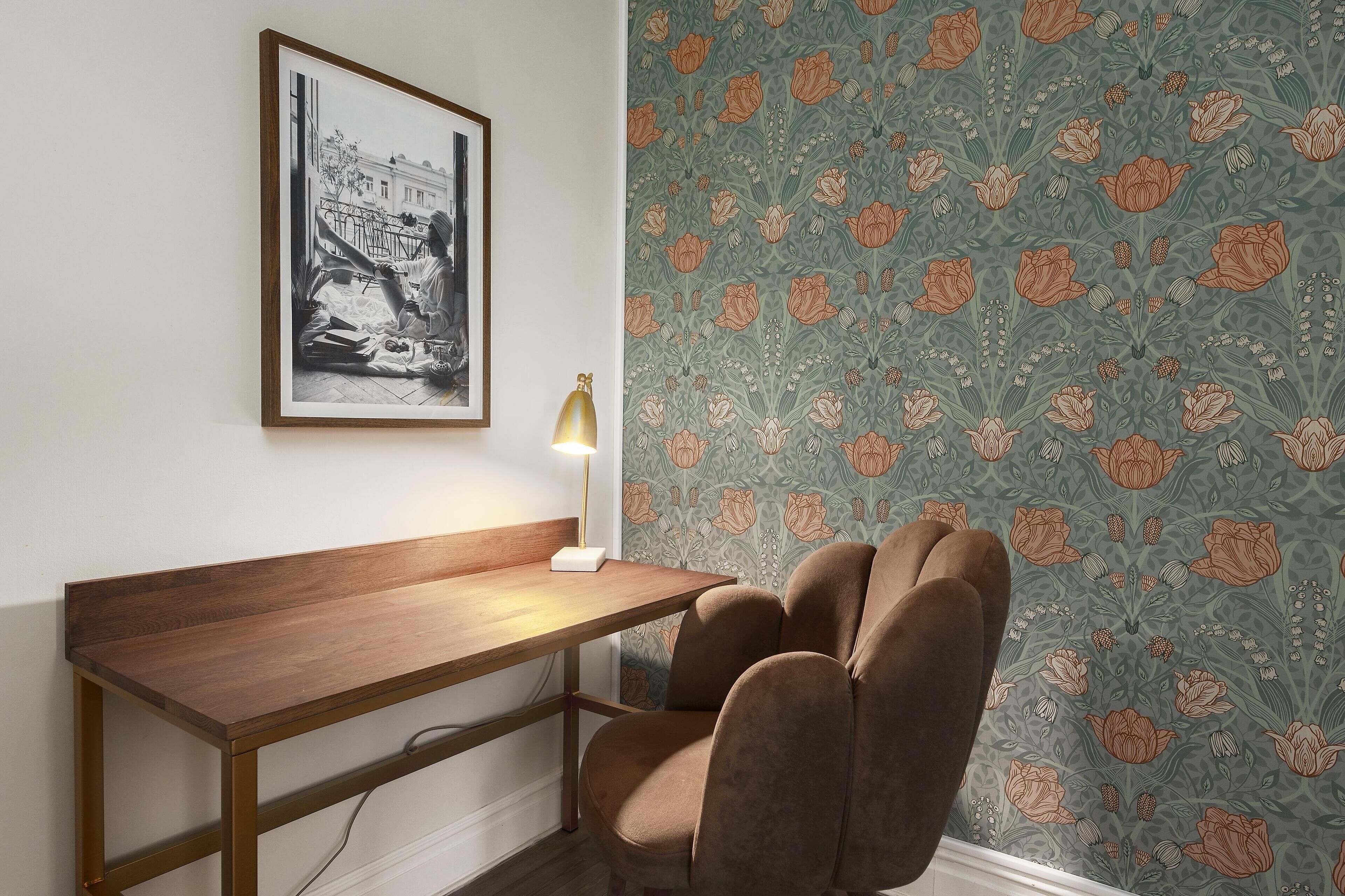 Une pièce avec un bureau en bois, un tableau encadré au mur et un papier peint à motifs.