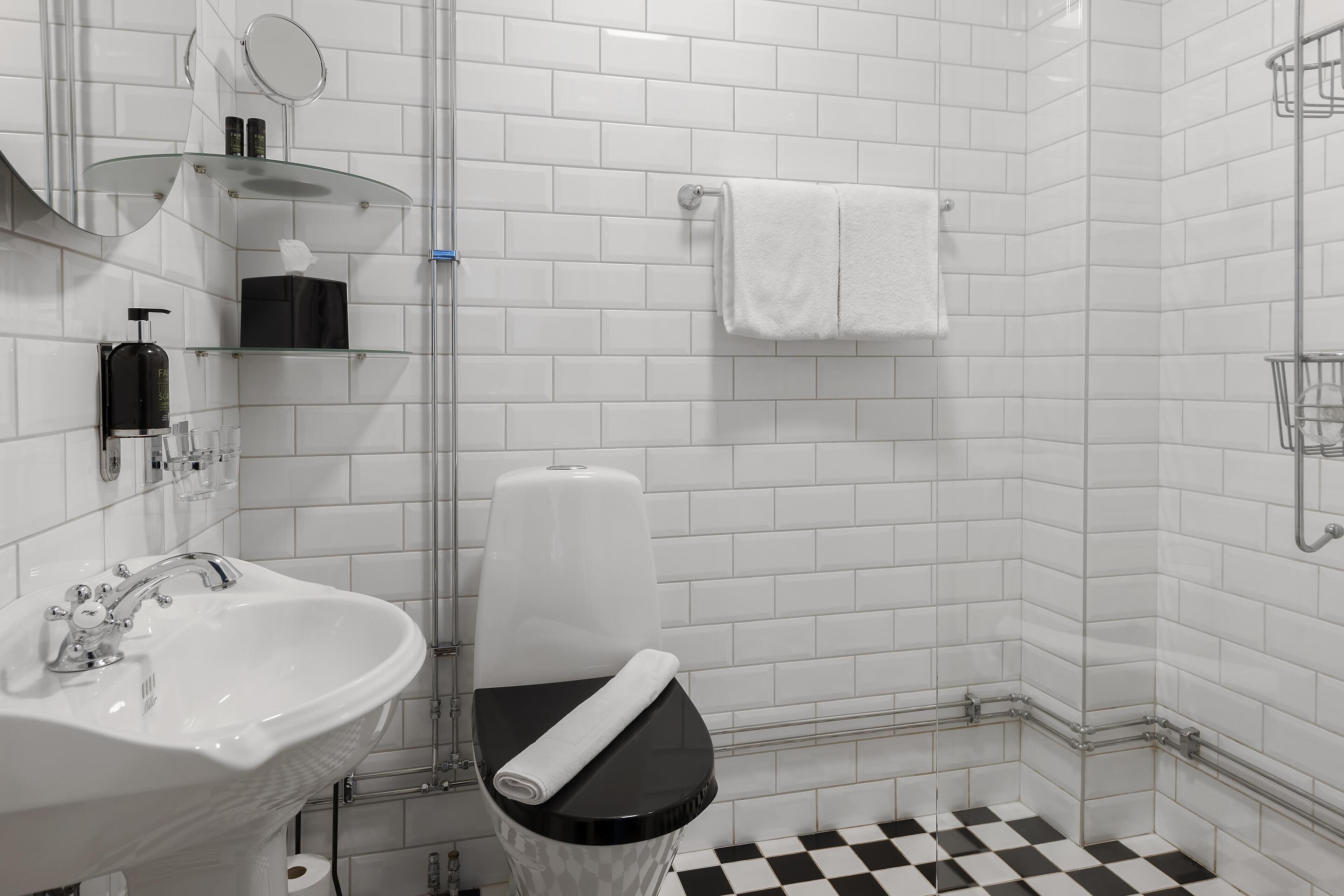Un baño moderno con un lavamanos blanco, inodoro negro y baldosas de piso a cuadros.