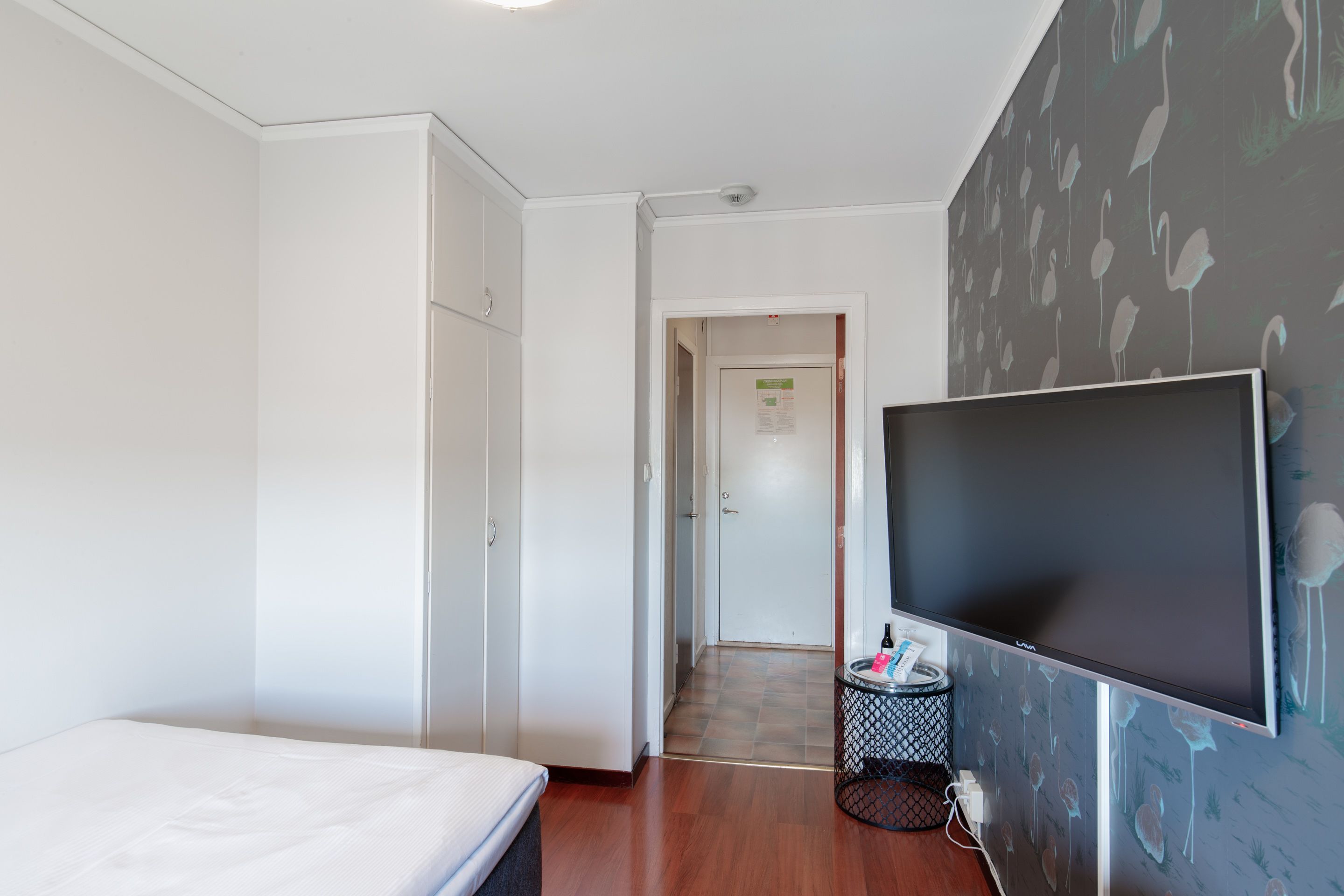 A hotel room with a bed, a wardrobe, a television, and a wall with a bird pattern.